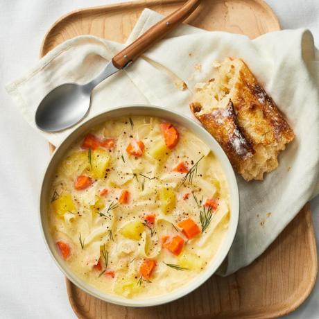 Un bol cu ​​supă cremoasă de cartofi, varză, lângă o lingură și o bucată de pâine prăjită