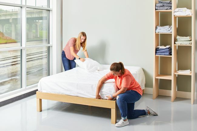 două femei făcând pat cu cearșafuri albe